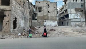 Eine Frau und ihr Kind laufen vor zertrümmerten Häusern in Homs