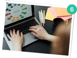 Hände tippen auf einem Laptop, auf dem ein Diagramm auf dem Bildschirm zu sehen ist, umgeben von bunten Stiften, Haftnotizen und einer schwarzen Tasse.