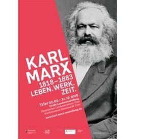 Schwarz-weiß-Foto von Karl Marx mit rotem Hintergrund und Text zu seinem Leben und Werk.